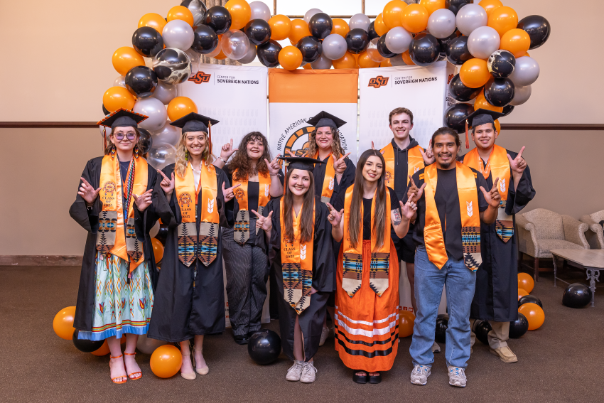 NASA students pose in graduation stoles in front of orange and black balloon arch with 