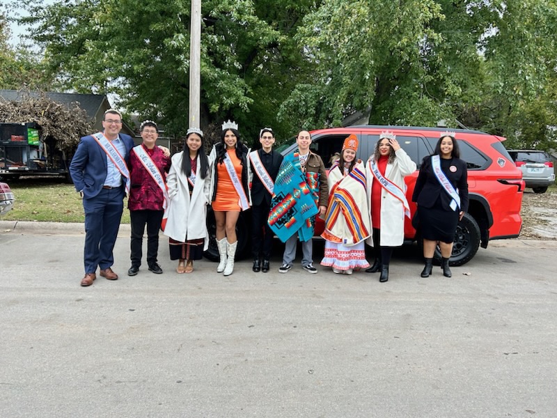 Miss American Indian OSU Shaeleigh and Mister American Indian OSU Caleb, both wearing Pendleton blankets, standing with all 2023–2024 OSU pageant royalty at the OSU Homecoming Parade.