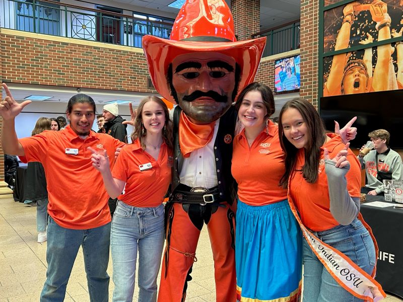 Miss American Indian OSU Shaeleigh pictured at a Center for Sovereign Nations tabling event with CSN employees Josiah, Tylie, and Hayley, posing with Pistol Pete, all wearing matching orange CSN polos.